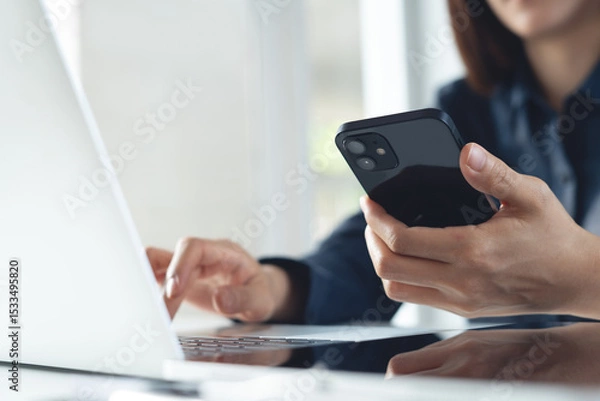 Obraz Young asian business woman using smartphone and working on laptop computer with digital tablet on office table. Businesswoman surfing the internet, closeup