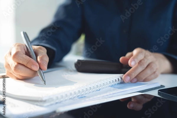 Obraz Close up, business woman writing in notebook while sitting at working place with laptop computer with financial report on office table. Businesswoman doing finance and making notes on notepad