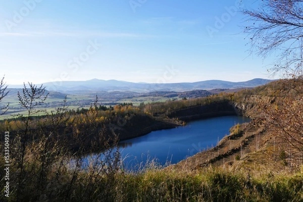 Fototapeta Panoramic view of serene blue lake surrounded by autumnal trees on rolling hills, vibrant landscape capturing stunning natural beauty under a clear sky with distant mountain range