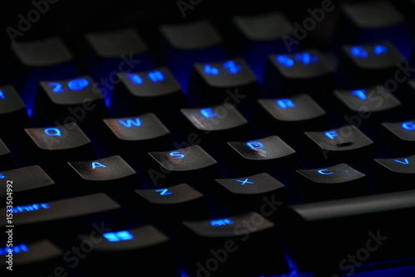 Fototapeta Close-up of illuminated mechanical keyboard keys with blue backlighting, showcasing technology and gaming equipment details for digital workspaces and gaming setups