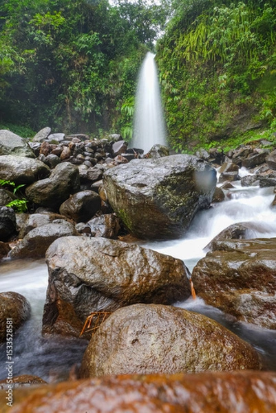 Obraz A serene waterfall cascades over rocks in a lush, green forest setting.