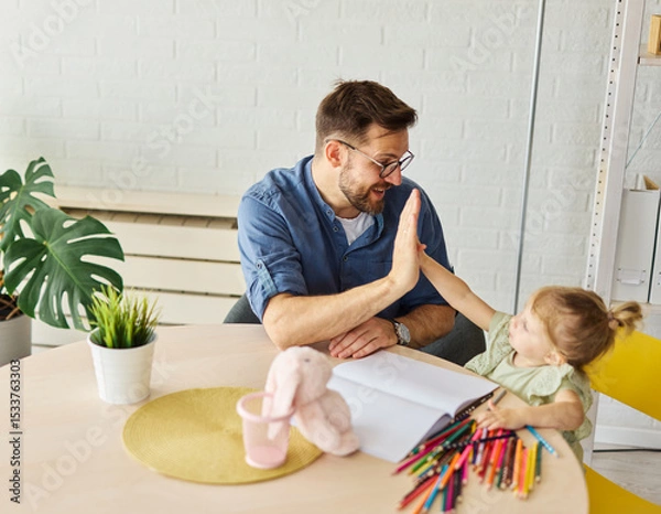 Fototapeta Portrait of a little girl and father or teacher coloring a book in classroom or at home. Education and development concepts