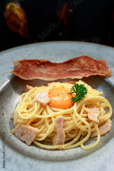 Fototapeta close up of a plate of pasta carbonara with a slice of bacon 