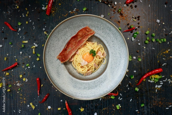 Fototapeta close up of a plate of pasta carbonara with a slice of bacon 