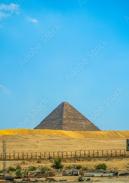 Fototapeta Iconic Egyptian pyramid structure emerging from sandy desert terrain with weathered limestone blocks