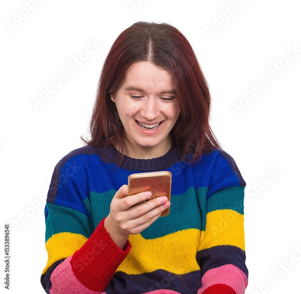 Fototapeta Cheerful woman wearing a colorful sweater holding smartphone browsing social media with a smile on her face, positive emotions. Modern technology artificial intelligence and virtual services network