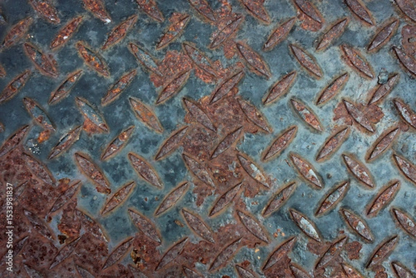 Fototapeta View of a heavily rusted diamond plate metal surface. The textured pattern is visible beneath layers of rich orange and brown rust, contrasted with patches of dark.