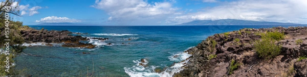 Fototapeta Panoramic view of a rocky coastline with blue ocean and sky.