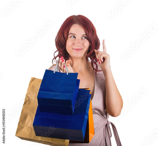 Fototapeta Redhead woman shopaholic trying to pay attention pointing forefinger up as has an idea. Looking thoughtful and sneaky female carrying shopping bags isolated on transparent background