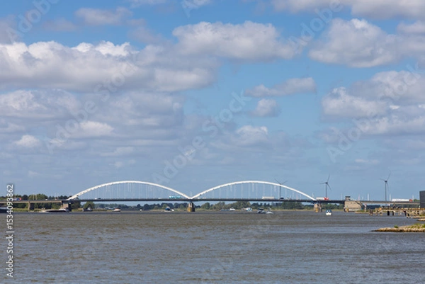 Obraz The majestic Merwedebrug Gorinchem (Merwede Bridge) spans a wide river under a bright, cloudy sky, showcasing modern infrastructure and Dutch waterways.