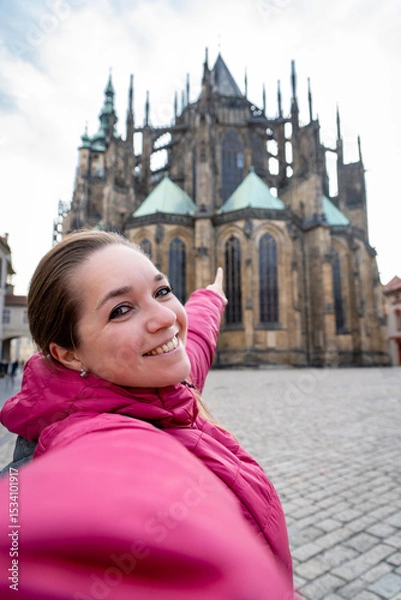 Obraz Mujer turista tomándose una selfie en frente de la Catedral de Praga, señalando hacia ella.