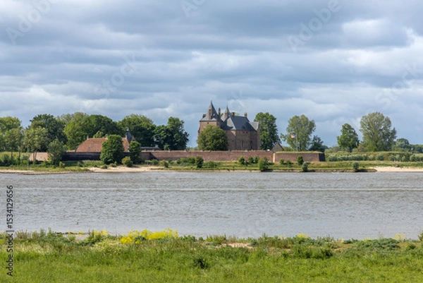 Obraz Historic Loevestein Castle, a medieval fortress in the Netherlands, stands majestically across a wide river under a dramatic cloudy sky.