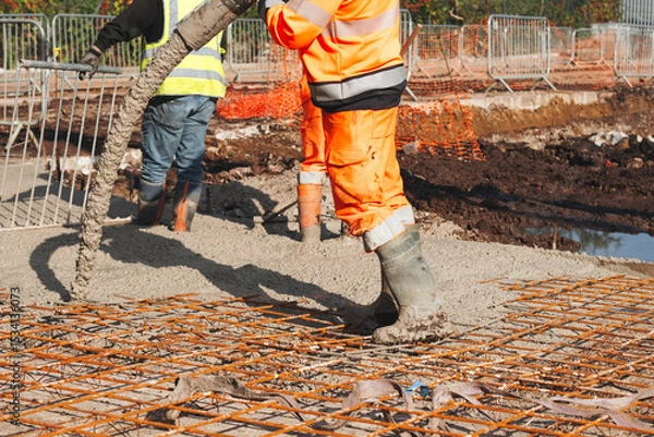 Obraz Construction worker pouring concrete onto reinforcing mesh at a building site