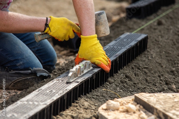 Obraz Construction workers installing drainage system channel components at building site
