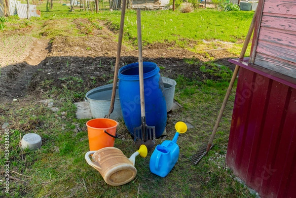 Fototapeta Garden buckets and watering cans of different colors in a suburban area near the wall of the house