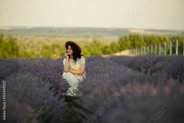 Fototapeta A young brunette walks in wheat fields at sunset in summer. Growing organic wheat and barley.