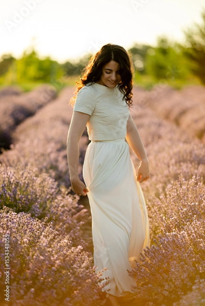 Fototapeta A young brunette walks in wheat fields at sunset in summer. Growing organic wheat and barley.