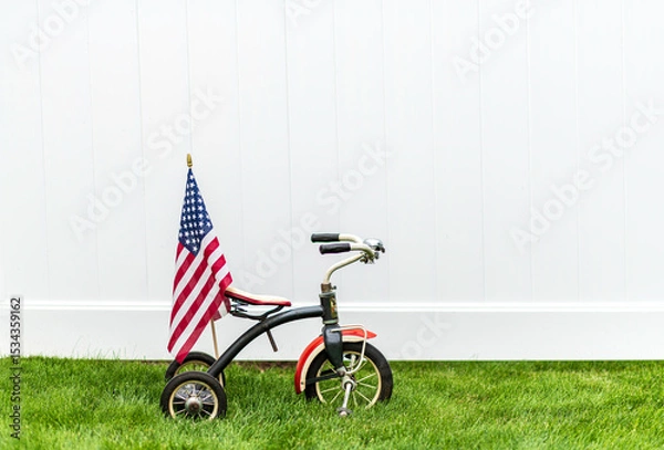 Obraz vintage tricycle with American flag on green grass with horizontal white background and room for copy
