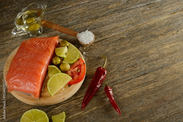Fototapeta Meat red salmon fish, tomatoes, spices, lemon, green olives and olive oil on wooden kitchen table.