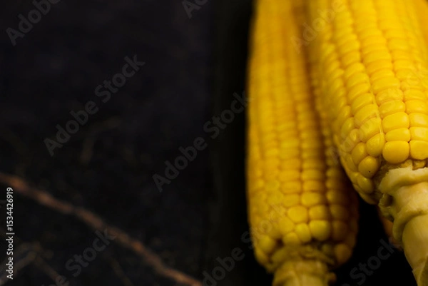 Fototapeta Close-up of honor yellow ripe peeled corn cobs with large grains and trunk legs on a dark background with space for text. The concept of healthy nutrition, natural iron, corn cultivation. High quality