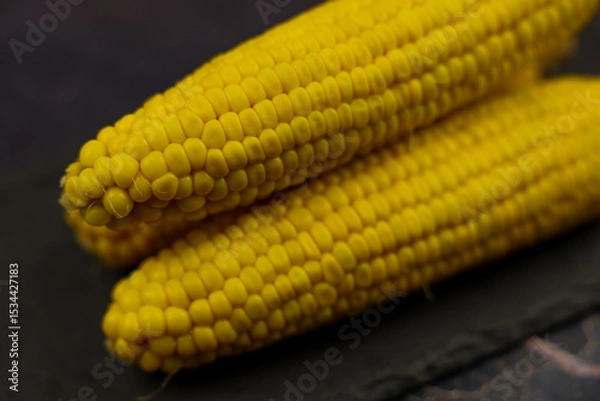 Fototapeta Close-up of yellow, ripe, peeled ears of corn with large grains lying sideways against a dark background in the center. The concept of healthy nutrition, natural iron, corn cultivation. High quality