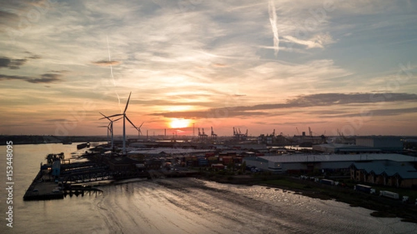 Fototapeta Dusk at the Port of Tilbury, Essex, UK. Sunset view of the low tide of the River Thames and wind turbines turning in the background.