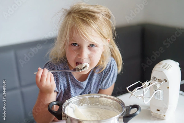 Obraz Young girl enjoys sweet cream while baking in a cozy kitchen during the afternoon