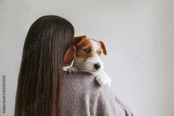 Obraz Back view of a brunette woman holding a dog. Copy space background.