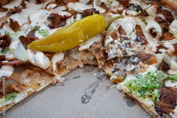 Obraz Close-up of partially eaten doner kebab pizza with creamy sauce and pickled pepper in a box