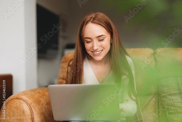 Obraz Young woman enjoying leisure time while using a laptop on a comfortable couch in a cozy indoor space during the day