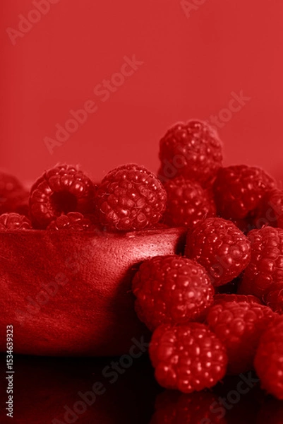 Obraz Raspberries in a red wooden bowl against a red background backdrop.