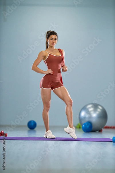 Fototapeta sporty girl showcases her athletic figure in a gym environment, striking a pose while surrounded by fitness equipment, radiating confidence and motivation