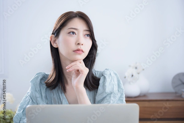 Fototapeta 部屋でパソコンをみて考える悩む迷うかわいい女性　ちょっと真剣なネガティブイメージ　転職どうしようかな～