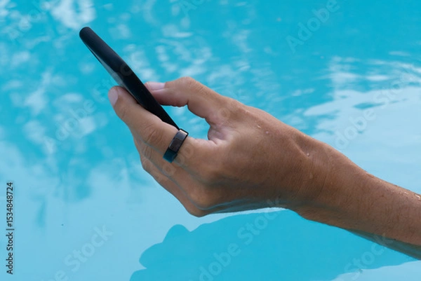 Fototapeta Hands in pool water wearing black smart ring and using smartphone. 
