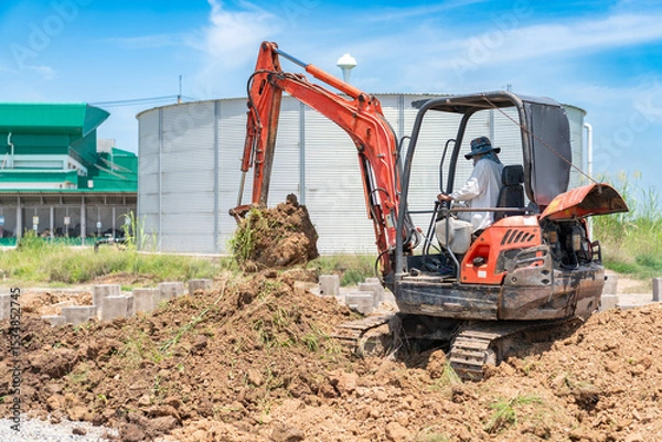 Fototapeta The mini excavator is scooping the stockpiled soil to backfill the piles.