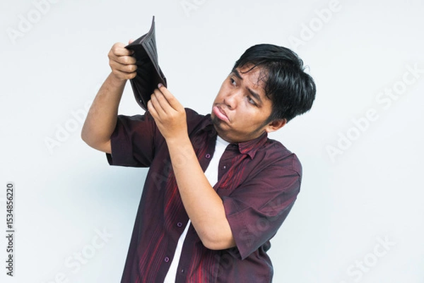 Obraz Asian Indonesian man showing his empty wallet with sad and worried expression. Isolated in gray background.