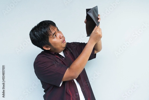 Obraz Asian Indonesian man showing his empty wallet with sad and worried expression. Isolated in gray background.