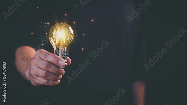 Fototapeta Young man holding a glowing light bulb in a dark background, symbolizing creativity, creative solutions, innovation, and bright ideas. Business global internet connection application technology.