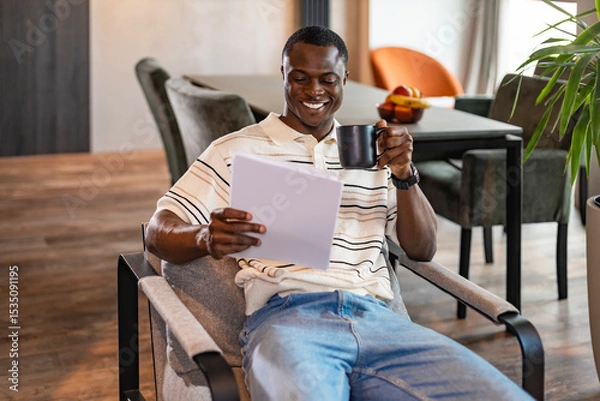Fototapeta A serious young african entrepreneur accountant, financier, analyst, auditor sits at home at the table. He types on a laptop.