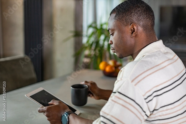 Fototapeta Smiling handsome african man using tablet with social networks at home, happy freelancer making online shopping