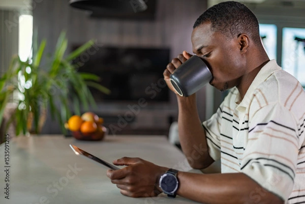 Fototapeta Smiling handsome african man using tablet with social networks at home, happy freelancer making online shopping
