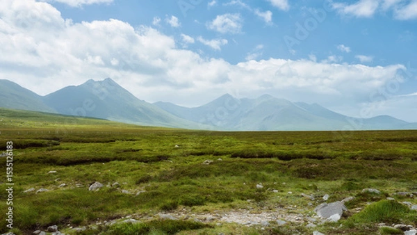 Fototapeta Rolling green hills meet dramatic, dark mountains under a brooding, cloudy sky. A peaceful, yet powerful landscape.