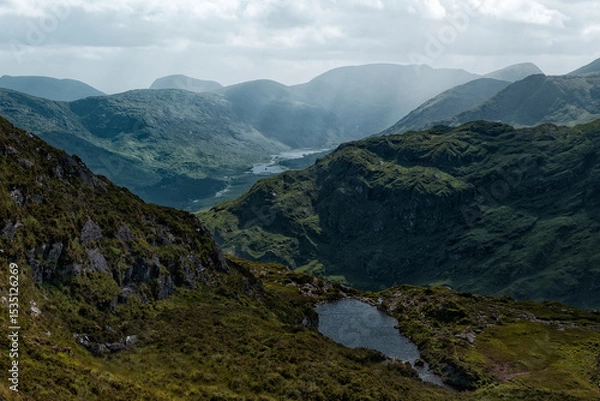 Fototapeta A small lake sits on the hillside, overlooking the beautiful Gap of Dunloe valley. Rolling green mountains stretch into the distance in County Kerry, Ireland.