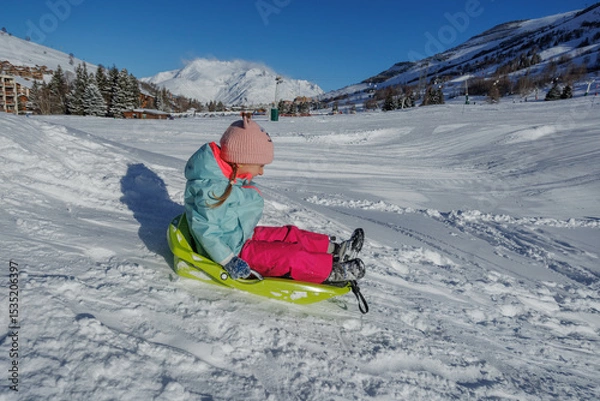 Obraz Little girl in pastel coat slides down on green sled, have fun