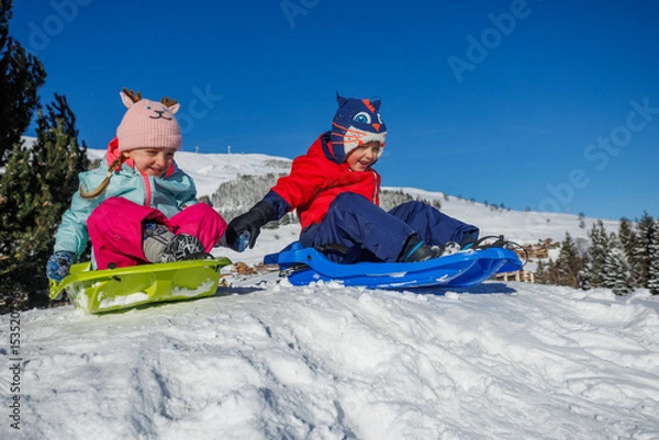 Obraz Joyful children sledding on a snowy hill, bundled and happy