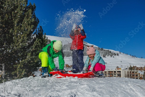 Obraz Kids have fun tossing snow overhead resort chalets behind them