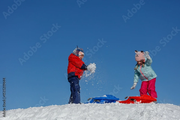 Obraz Two children in bright coats throw snow at each other on hilltop