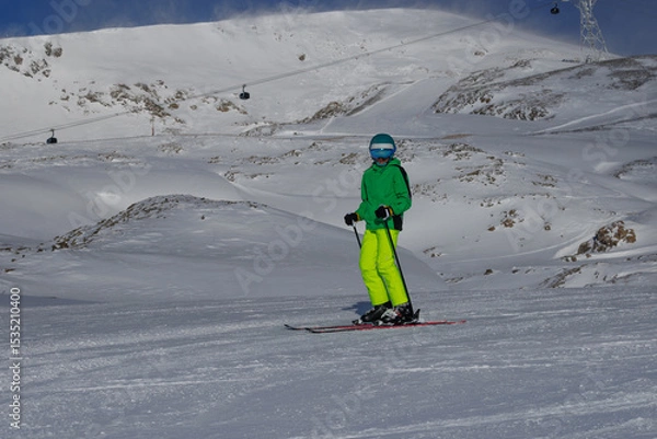 Obraz Skier in green jacket stands on red skis overlook alpine valley
