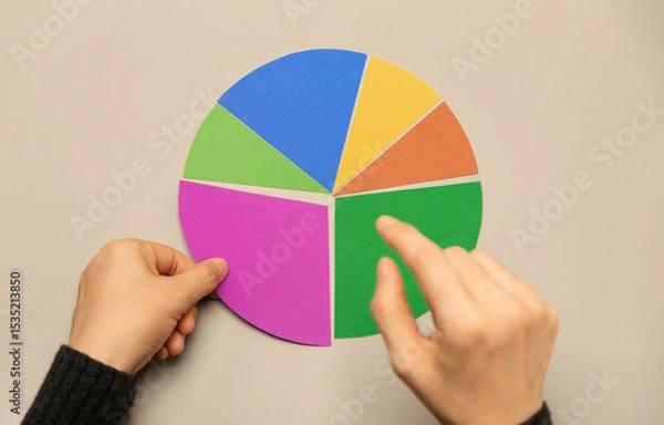Fototapeta Hand selecting a segment on a colorful pie chart representing data analysis, investment portfolio allocation, and strategic financial planning