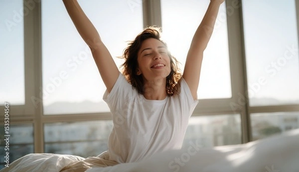 Fototapeta Woman stretching in her bed with joyful and relaxed expression, enjoying bright morning in modern room with large windows and natural sunlight. scene exudes happiness and freshness
